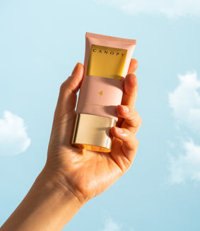 Hand holding CANOPY skincare tube against sky, showcasing sustainable and recyclable packaging.