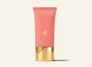 Coral-colored skincare product tube with gold cap on a light beige background