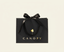 A black CANOPY shopping bag with a black ribbon bow and gold lettering, centered on a light cream background.