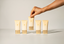 Five CANORY hand cream tubes in a pale peach-beige color with gold caps are lined up on a light gray surface, with a hand reaching to lift the center tube.
