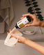 Person applying a product from a bottle onto a cloth in a bathroom setting