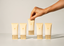 Five CANOFY skincare tubes in a warm cream color with gold caps are lined up on a white surface, with a hand reaching to pick up the center tube against a clean white background.