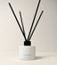 A reed diffuser bottle in matte white with black reeds, on a clean off-white background. The bottle is labeled 'CANOPY '   gift for the home