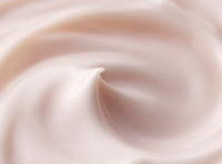 A close-up texture shot of a creamy, pale pink cosmetic cream with smooth, flowing swirls.
