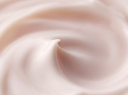 A close-up texture shot of a creamy, pale pink cosmetic cream with smooth, flowing swirls.