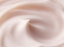 A close-up texture shot of a creamy, pale pink cosmetic cream with smooth, flowing swirls.